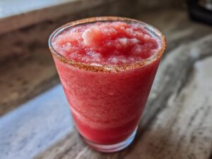 Close-up of a vibrant red frozen firecracker rosé slushie with a chili-lime rim.