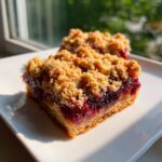 A close-up of a square slice of german plum cobbler bar with a thick, jammy filling and golden crumble topping.