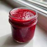 Close-up of vibrant, deep red raspberry vinaigrette mixture filling a small glass jar.