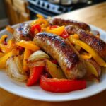 Close-up of browned sausages served with roasted peppers, onions, and potatoes.