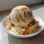 A perfect scoop of creamy apple pie ice cream drizzled with caramel sauce in a white bowl.