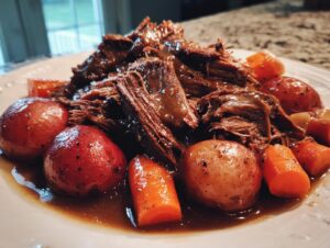 Close-up of tender, shredded slow cooker pot roast served with whole red potatoes and chopped carrots in rich gravy.