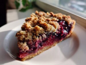 A close-up of a delicious slice of german plum cobbler featuring a thick, jammy plum filling and a golden brown streusel topping.