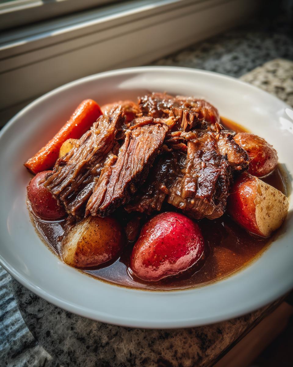 A bowl filled with shredded slow cooker pot roast, red potatoes, and carrots swimming in rich brown gravy.